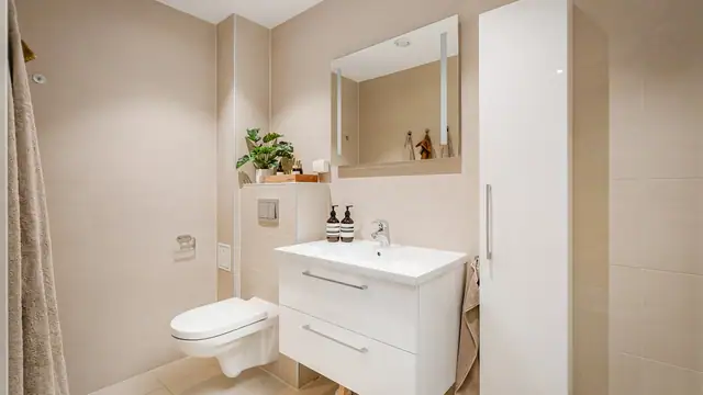 Praktisk og pent Baderom med innredning, nedfelt servant og veggmontert toalett og vaskemaskin/tørketrommel.