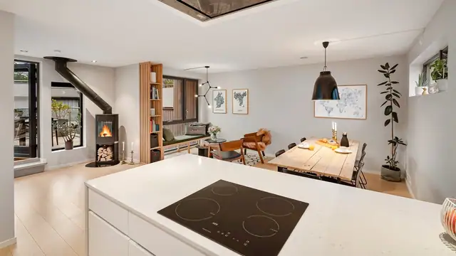 Fra kjøkkenøyen har man kontakt med spisestuen, oppholdsstuen og vedovnen, samt direkte adkomst til terrassen.